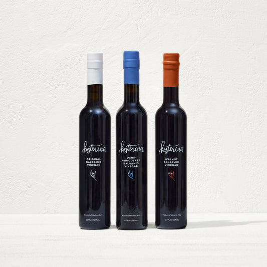 Three bottles of 'Kosterina' vinegar with different colored caps on a white background